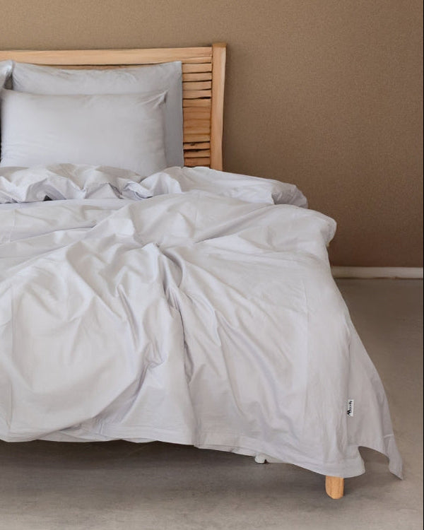 Bed with white bedding and light gray pillows against a beige wall.