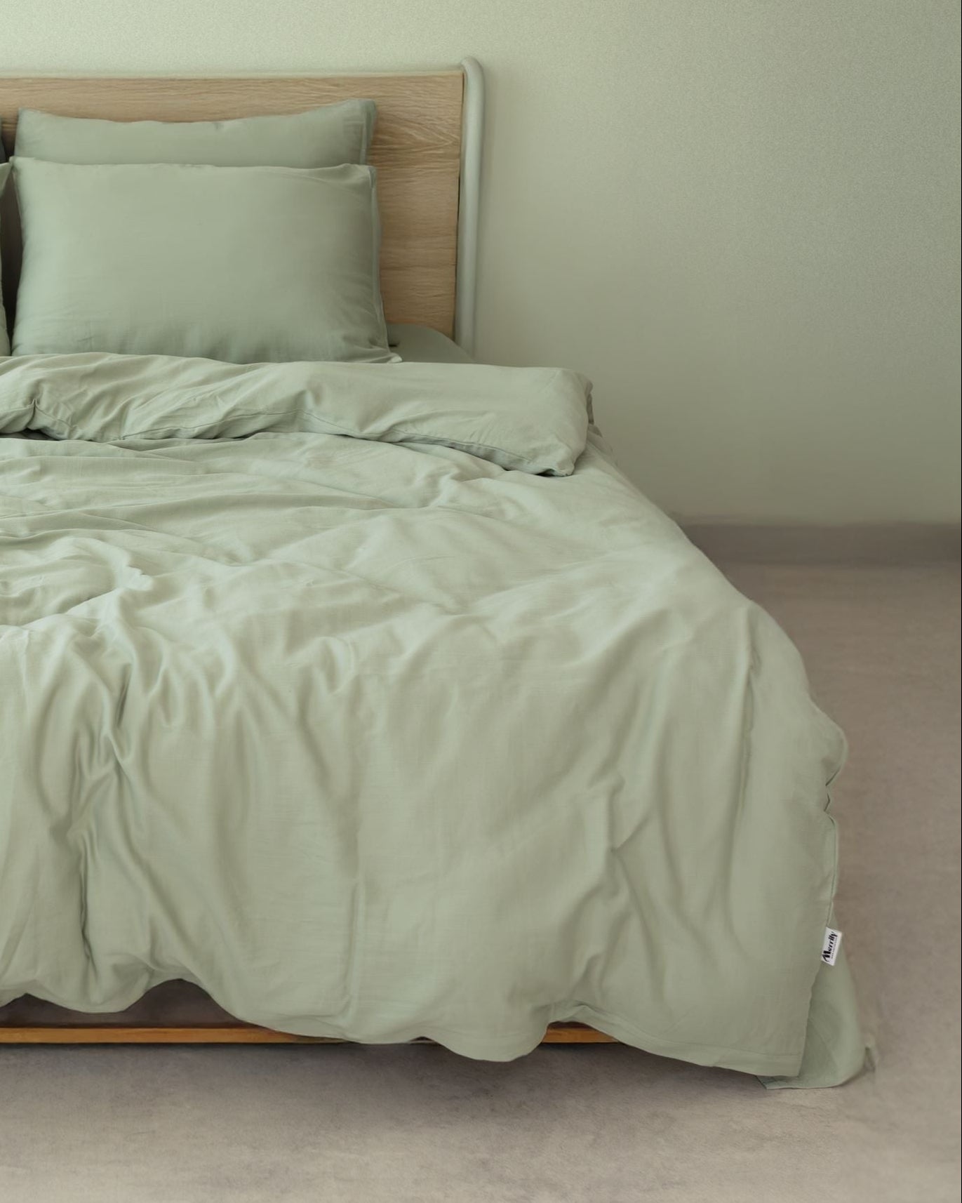 Bed with green bedding and pillows against a plain wall